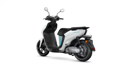 White and black scooter shown from a rear-left angle, exposing the rear wheel and seat area (informative product image).