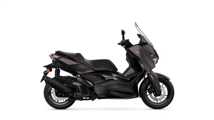 Side view of a dark burgundy Yamaha XMAX scooter with a tall windshield and disc brakes visible at the front wheel