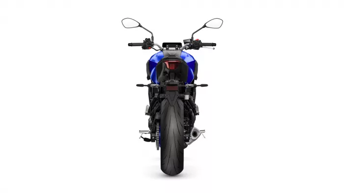 Rear view of a blue motorcycle, showing tail light, seat, and wide rear tire against a white background.