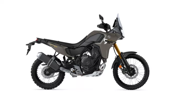 Side view of a Yamaha Tenere 700 adventure motorcycle in matte tan and gray with knobby tires and tall windscreen