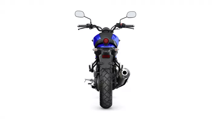 Rear view of a blue motorcycle showing the taillight, exhaust, and wide rear tire against a white background study.