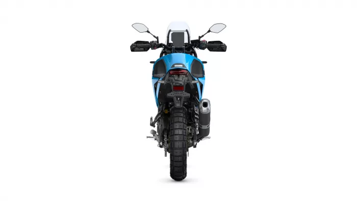 Rear view of a blue adventure motorcycle, showing the taillight, rear fender, exhaust, and wide rear tire with a tall windscreen above the cockpit