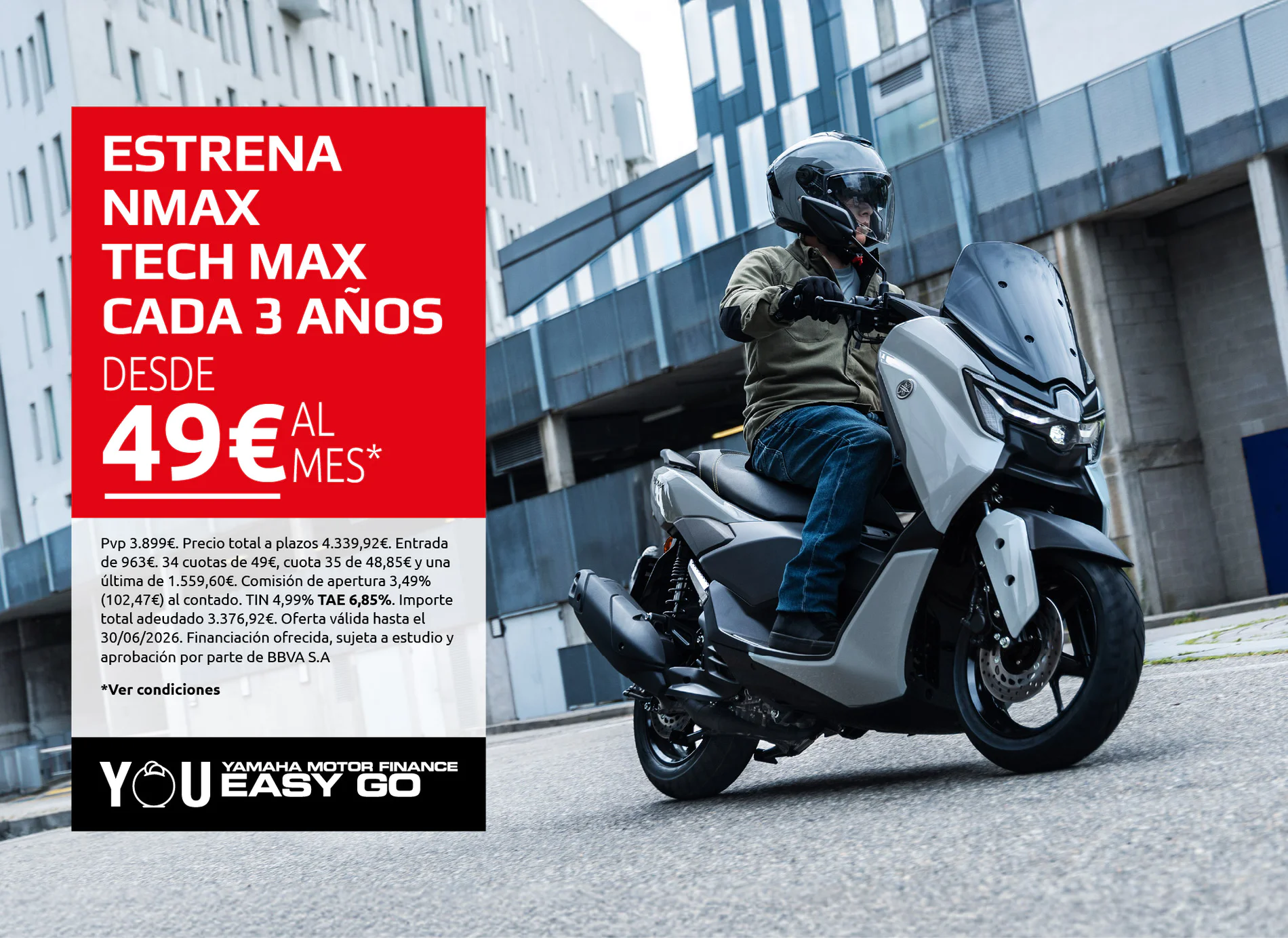 Motorcycle rider on a silver Yamaha scooter beside a large red promotional banner in an urban setting.