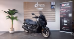 Black Yamaha scooter on a showroom floor, with a wooden slat wall and Dandy Moto branding in the background.