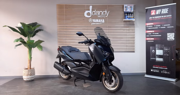 Black Yamaha scooter on a showroom floor, with a wooden slat wall and Dandy Moto branding in the background.