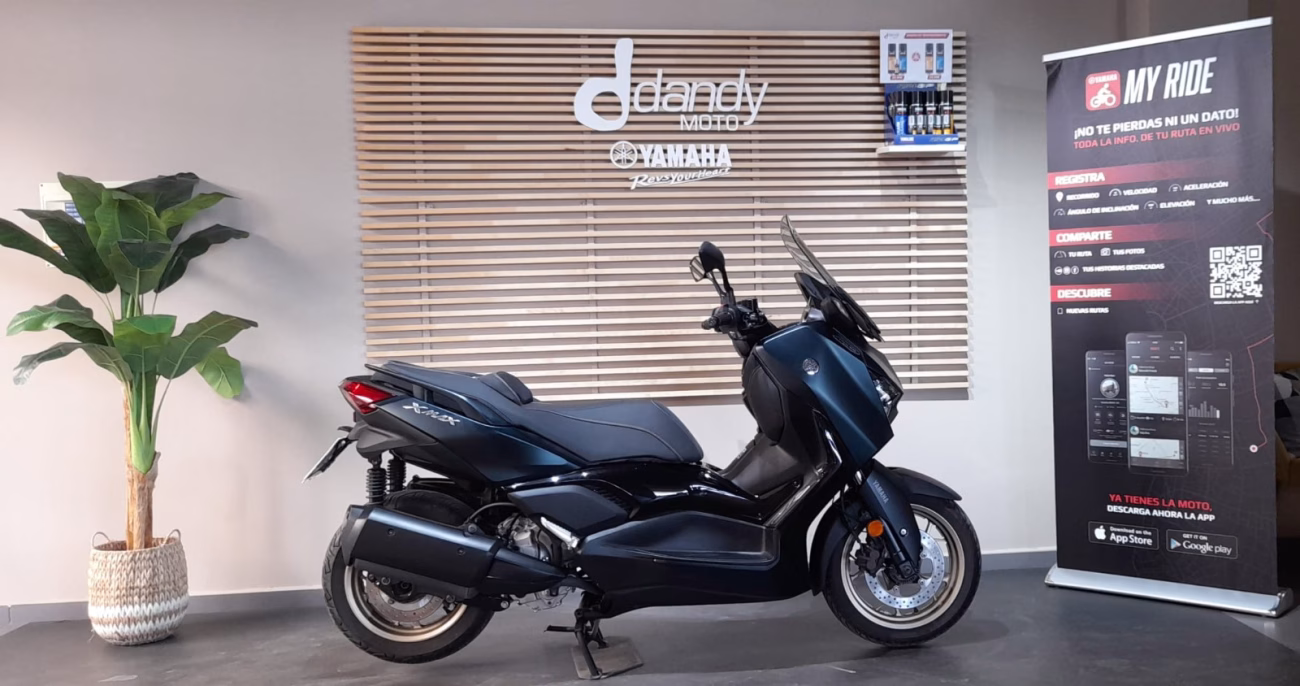 Black Yamaha scooter on display in a showroom with a wooden slat wall and nearby promotional banner.